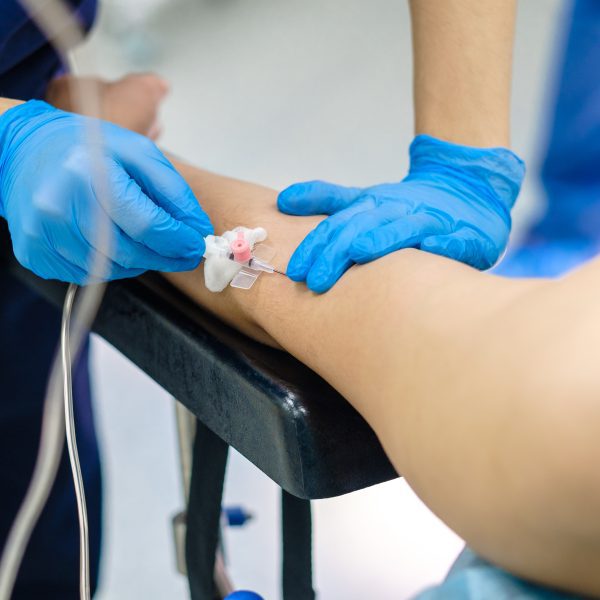 Installing a catheter for a medical dropper in the patient's arm. Selective focus. The doctor in sterile gloves puts the patient on a drip for intravenous administration of drugs.